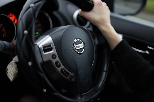Close-up shot of a person's hand gripping a Nissan steering wheel. Modern car interior.